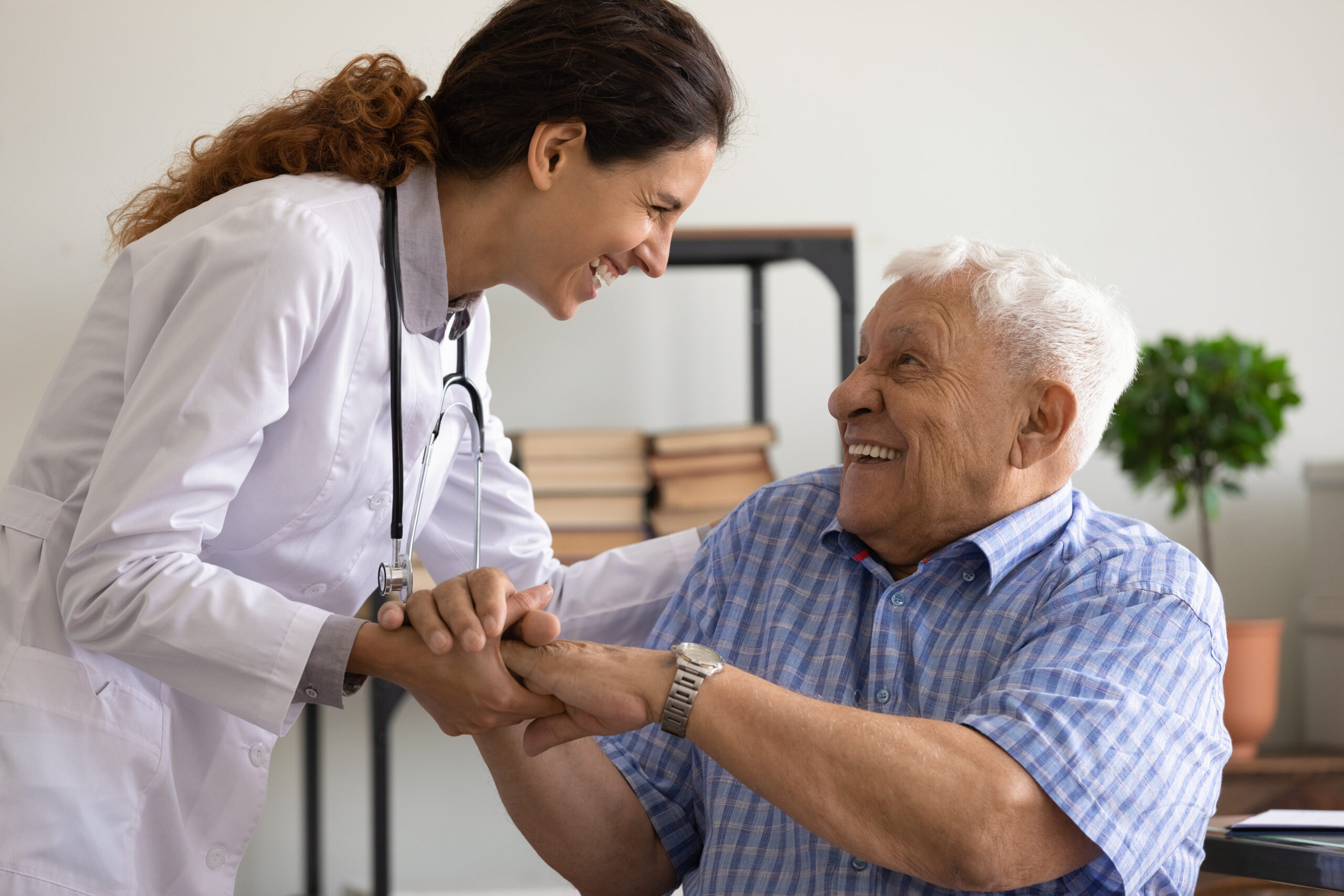 A smiling doctor holding the hands of a happy elderly man sitting at a desk, sharing a warm moment together.