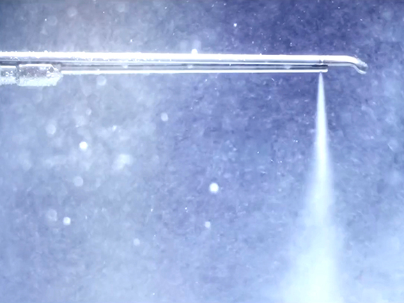 A surgical tool releasing a waterjet against a blurred, blue-gray background.