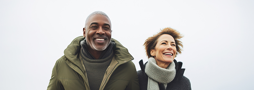 A man and a woman, both in winter clothing, smile as they walk on a foggy beach.