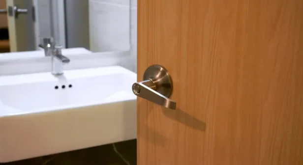 A partially open door revealing a white bathroom sink with a metal faucet in the background.